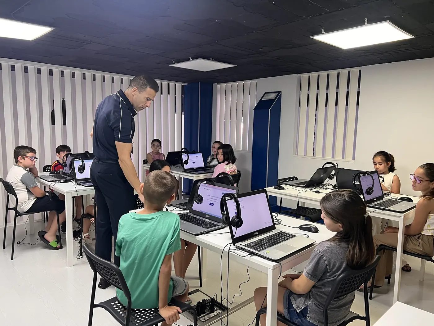 Un profesor ayuda a un alumno durante el examen digital de Cambridge, con portátiles y auriculares.