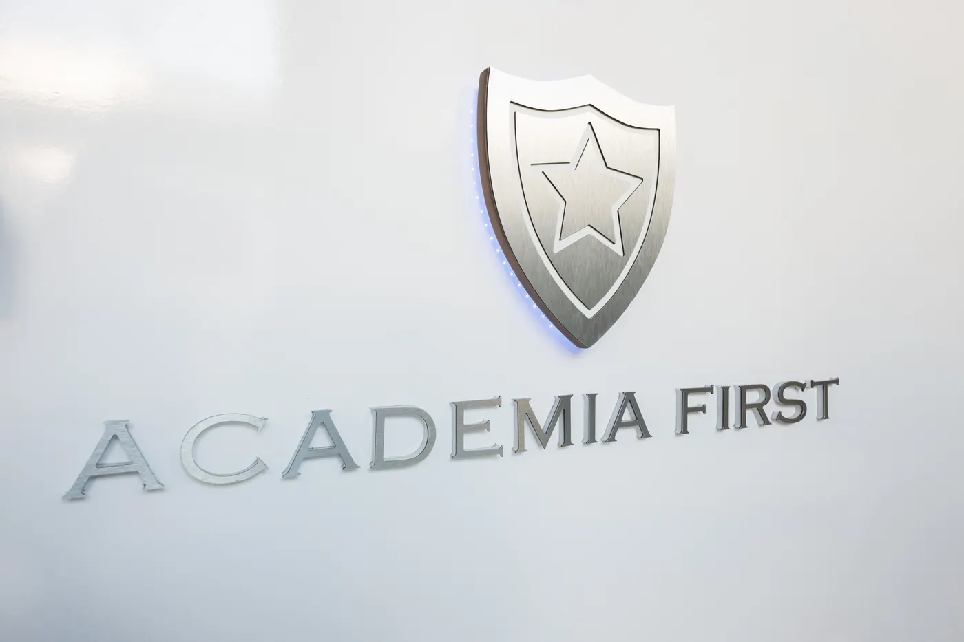 Escudo metálico y letras de Academia First en el mostrador.