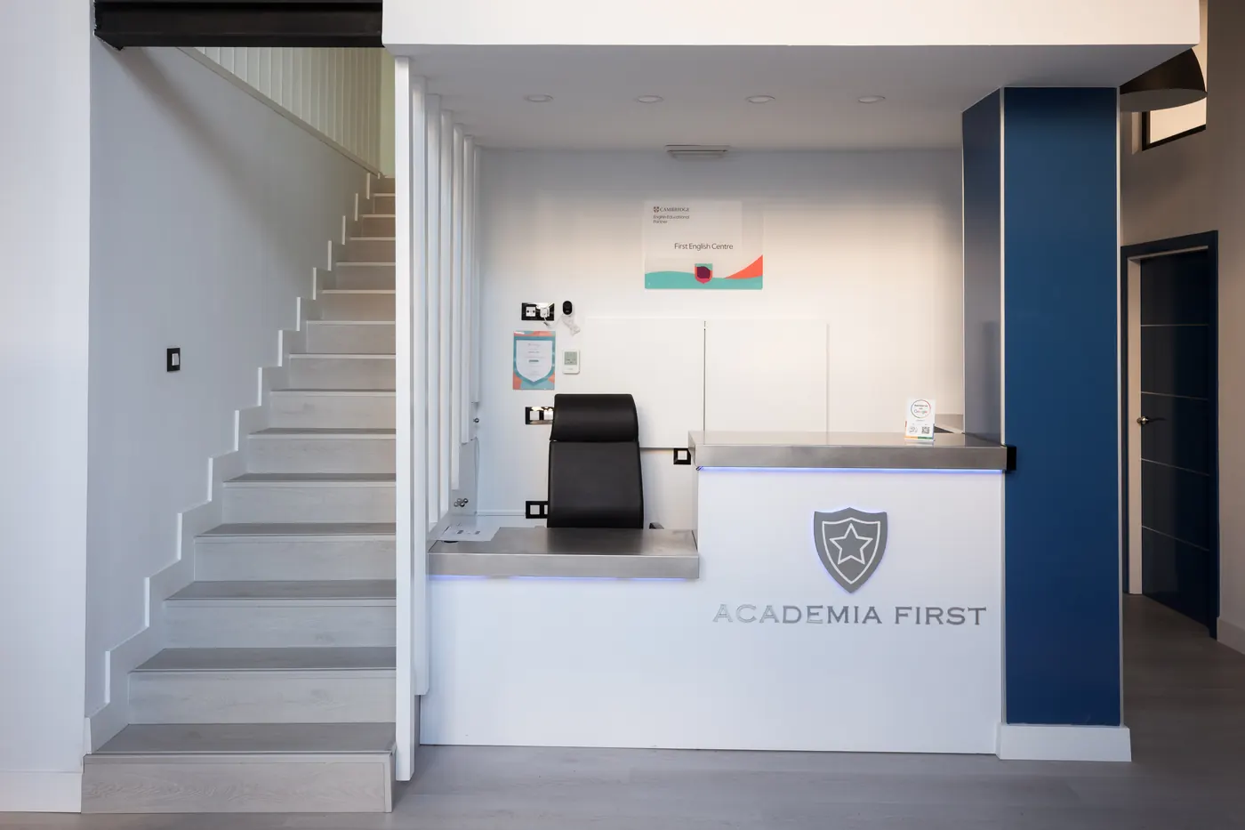 Recepción de First English Centre, con el mostrador iluminado y la escalera de los niveles.