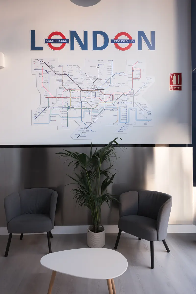 Zona de espera con dos sillones grises, una mesa baja blanca, una planta y, en la pared, el mapa del metro de Londres.